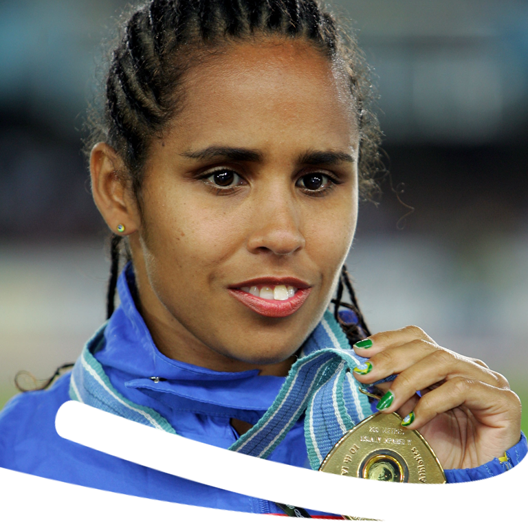Foto de Adria Santos sorrindo com uniforme azul segurando medalha pendurada no pescoço.